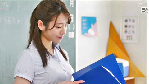 Cute Japanese brunette student with long ponytail smiling while holding blue folder in classroom