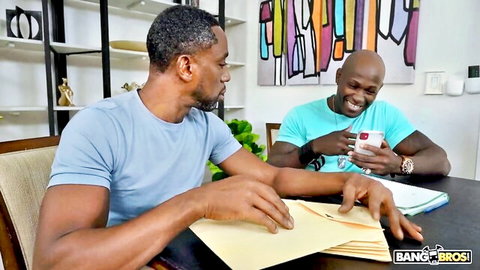 Two muscular black men in blue shirts sitting at table reviewing papers in Bang Bros scene