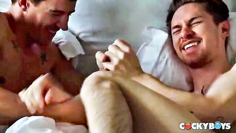 Tattooed athletic white guy roughly grabs and spreads muscular partner's ass during intense gay anal fuck on bed