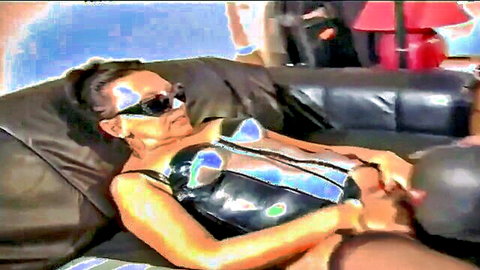 MILF in shiny black lingerie and sunglasses dominating slave on couch