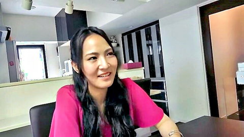 Smiling Asian woman in pink top sitting at office desk