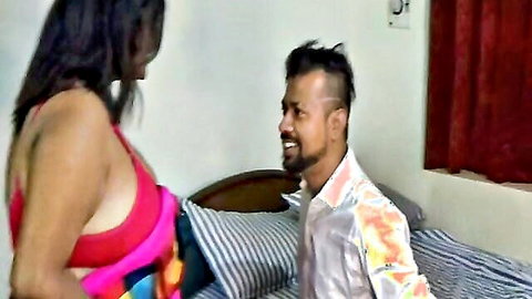 Busty Indian woman in tight pink top flaunts massive cleavage seducing smiling man on bed