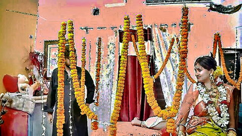 Beautiful Indian bride in orange saree with marigold garlands sitting during wedding ritual with groom in decorated room