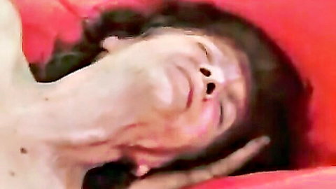 Mature woman with curly dark hair, topless neck close-up on red sheets
