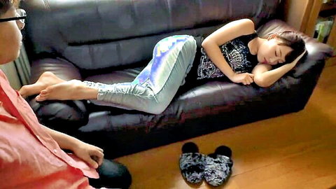 Asian wife sleeping soundly on couch in black tank top and shiny pants, unaware man watches