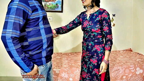 Clothed Indian couple standing intimately in bedroom, smiling woman in floral dress touched by man
