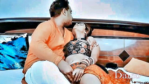 Indian man passionately kissing busty woman in black bra and orange skirt on bed