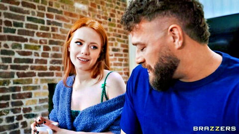 Redhead with freckles in open cardigan smiles at bearded muscular man in blue shirt