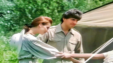 Redhead woman in safari outfit with hunk by jungle tent in Tarzan scene