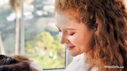 Sexy smiling redhead with curly hair and bare shoulders by window