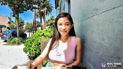 Cute Asian teen in pink crop top and shorts posing playfully outdoors