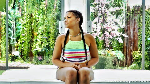 Sexy ebony babe with pigtail braids in colorful crochet bikini sitting teasingly on bed