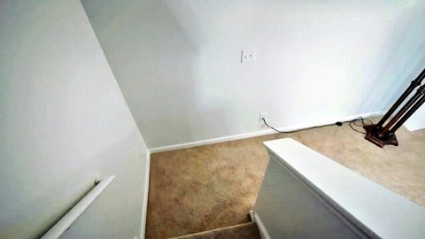 Empty white-walled staircase corner with beige carpet floor and wooden lamp