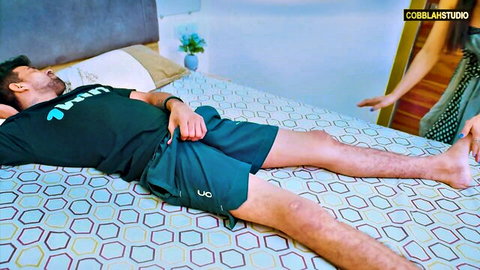 South Asian man lying on bed in t-shirt and shorts as woman in yellow top reaches toward him