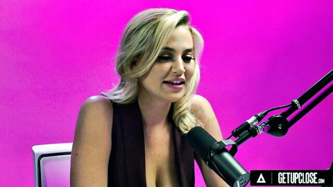 Blonde with huge tits in deep cleavage top speaking seductively into microphone