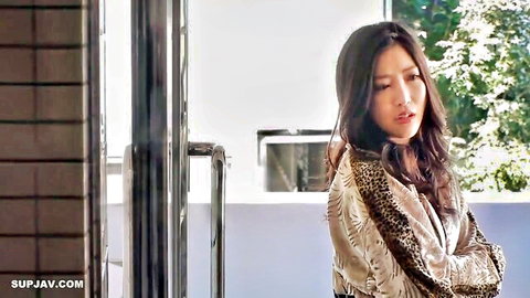 Young Asian brunette with long hair in leopard print blouse arms crossed on balcony
