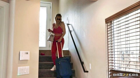 Pussy Queen in tight red leggings and sports bra, carrying suitcase down stairs