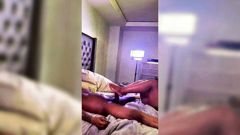 Ebony woman's dark feet pressing on naked man's crotch in blurry bedroom sex