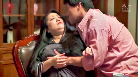 Asian man passionately kissing chubby long-haired Asian MILF while groping her tits on wooden chair