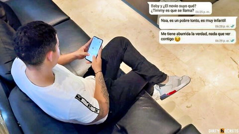 Latino guy lounging on leather couch reading flirty Spanish texts on phone