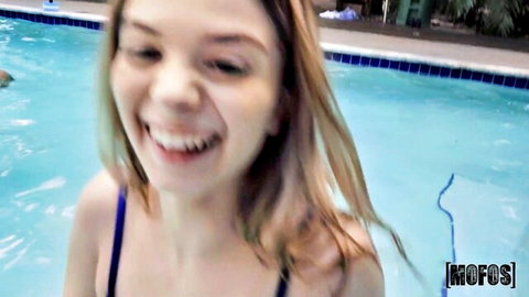 Smiling blonde teen babe in dark swimsuit posing playfully in pool POV