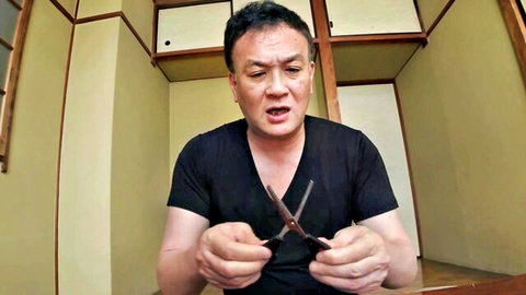 Japanese man in black shirt holding open scissors intensely in traditional room