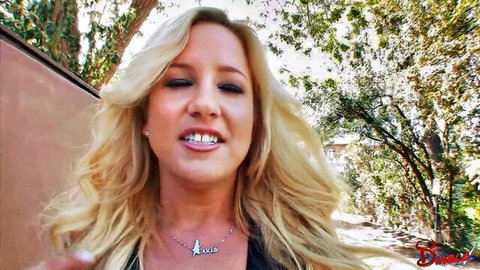 Blonde woman with long hair smiling seductively outdoors in black top showing cleavage