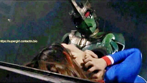 Supergirl in blue suit grabbed by neck by green armored villain in fight scene