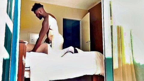 Muscular ebony hunk in tight white briefs bending over bed by open balcony