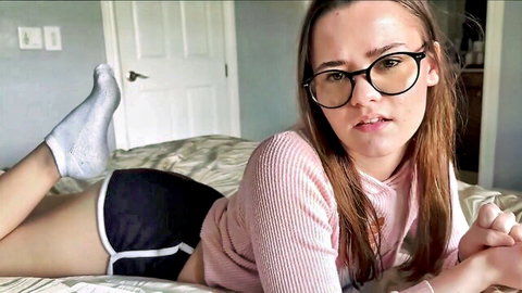 Skinny young brunette in glasses teases on bed lifting legs in tight shorts and sweater