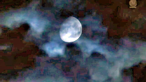 Blurry full moon partially obscured by dark swirling clouds in night sky