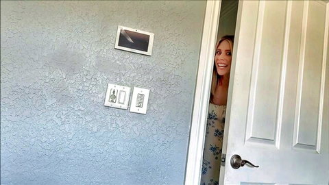 Blonde woman smiling excitedly peeking around bedroom door in floral dress