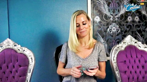 Blonde MILF in low-cut gray top smiling while checking phone with cleavage visible