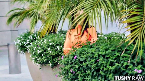 Ariana Marie peeking from bushes in red bikini, teasing outdoor vibe