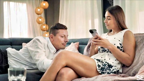 Milan Cheek in white dress with partner on couch, intimate phone moment