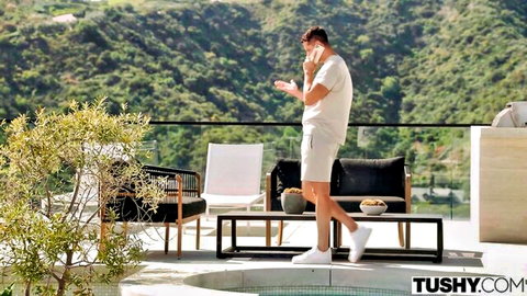 Handsome tanned man in tight white shorts talks on phone by luxury pool terrace