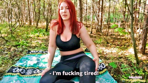 Curvy redhead PAWG with big natural tits in tight black sports bra and leggings sits on forest blanket