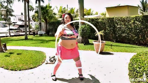 Brunette BBW in pink skirt hula hooping outdoors, teasing curvy figure