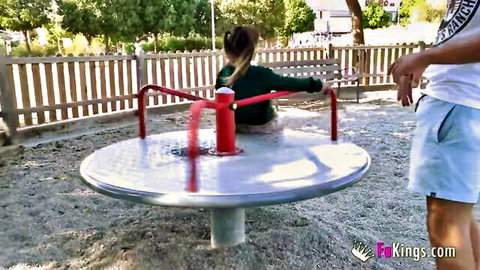 Petite midget girl Muequita on playground spinner with man nearby, teasing outdoor fun