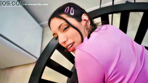 Sultry Latina in pink top with hair clips teases with tongue out on black staircase railing
