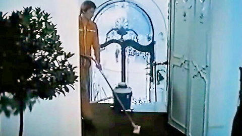 Young woman in orange uniform mopping floor in ornate vintage room