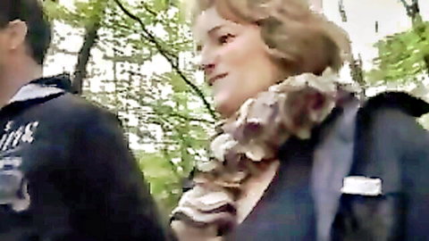 Mature blonde BBW woman in black jacket with ruffled scarf outdoors sunny day with man