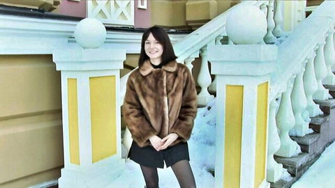 Young Asian woman in brown fur coat and black mini skirt on snowy outdoor stairs