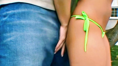 Jessica Darlin in skimpy green thong bikini, side view with lover's hand on hip