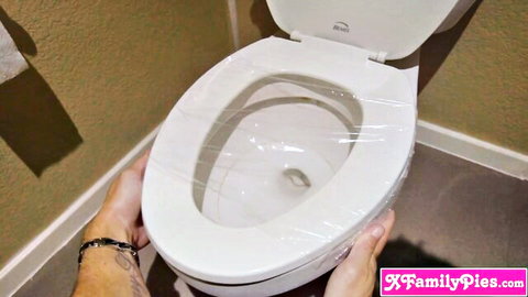 Hands gripping plastic-wrapped white toilet seat in bathroom closeup