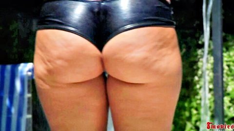 Tanned woman bends over exposing huge cellulite ass cheeks in shiny black latex shorts