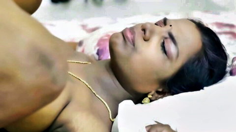 Indian MILF with big tits lying topless on bed, eyes closed moaning as man's hand gropes her nude breasts