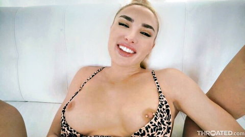 Smiling busty blonde with fake pierced tits exposes huge breasts in leopard print top on couch