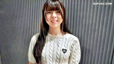 Cute Asian girl with bangs smiles seductively in tight white sweater showing heart logo