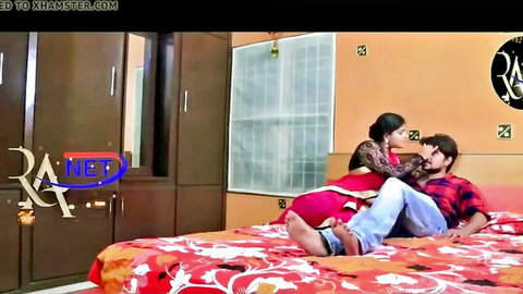 Sexy Indian woman in red saree passionately kisses man on bed in steamy foreplay.